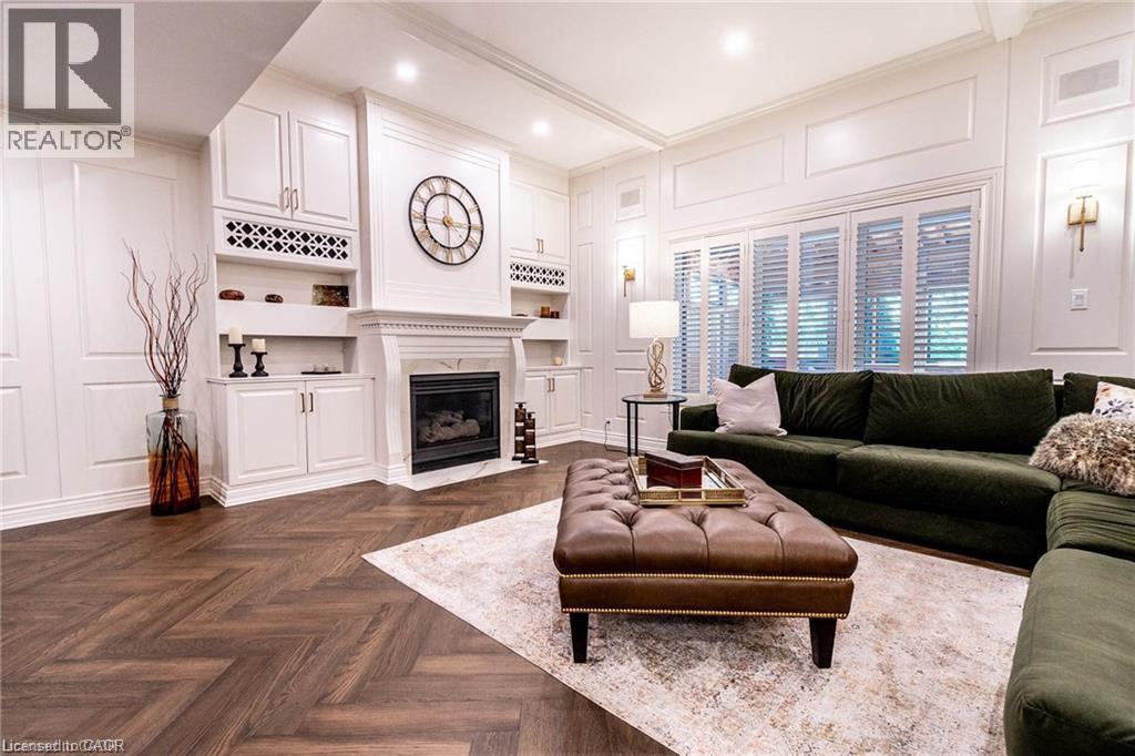 Living area featuring a herringbone wood-finish floor, built-in cabinetry, an integrated fireplace, decorative wall paneling, and interior window shutters - 76 Adriatic Boulevard, Hamilton, ON - Indoor Photo Showing Living Room With Fireplace
