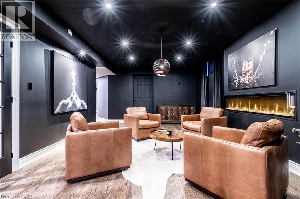 Media room featuring dark wall and ceiling finishes, recessed lighting, a linear electric fireplace, wood-finish flooring, and a pendant light fixture - 76 Adriatic Boulevard, Hamilton, ON - Indoor