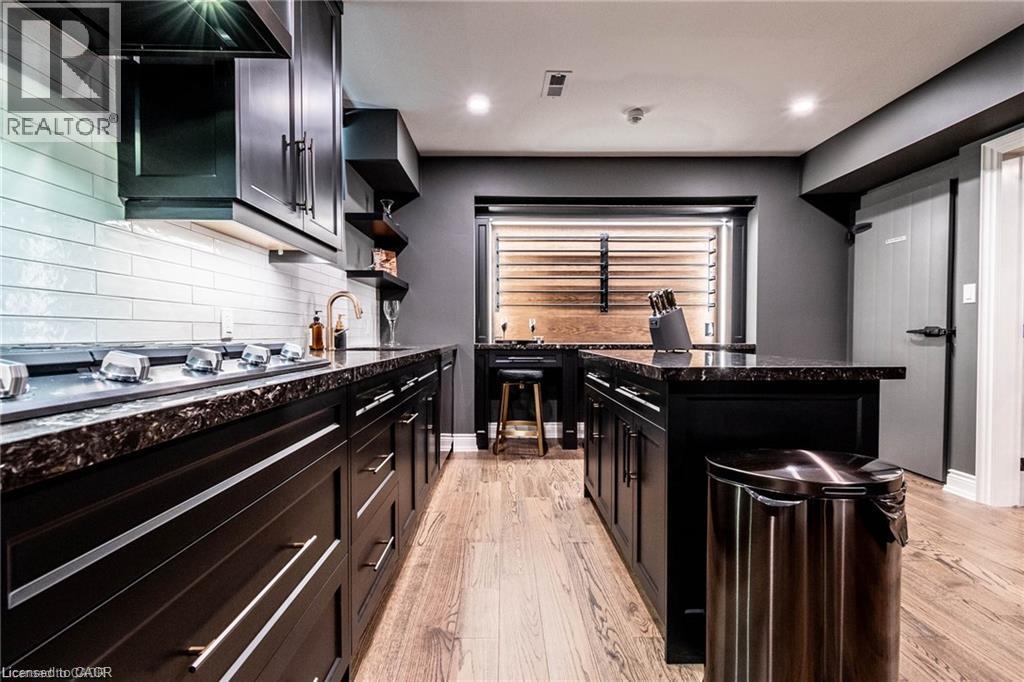 Contemporary kitchen featuring dark cabinetry with brushed nickel hardware, speckled countertops, a subway tile backsplash, and light wood-finish flooring - 76 Adriatic Boulevard, Hamilton, ON - Indoor Photo Showing Kitchen