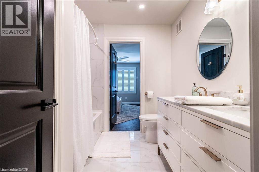 Contemporary bathroom featuring a spacious vanity with a stone countertop, an oval mirror, and a built-in shower with white tile surround - 76 Adriatic Boulevard, Hamilton, ON - Indoor Photo Showing Bathroom