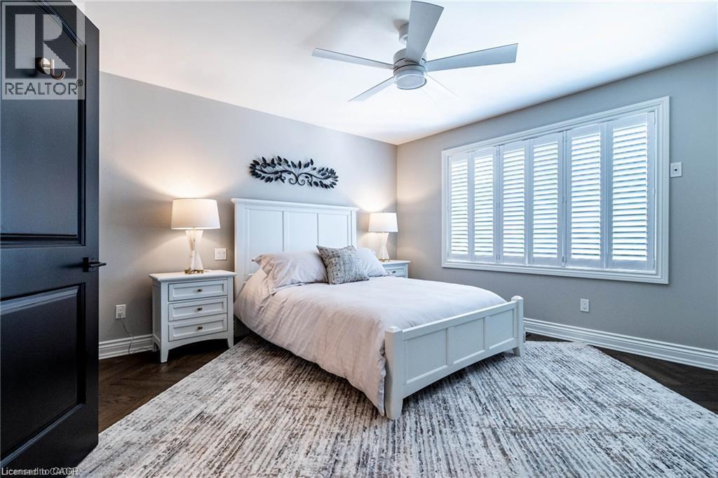 Spacious room featuring dark wood-finish flooring, a contemporary ceiling fan, and a wide window with white plantation shutters - 76 Adriatic Boulevard, Hamilton, ON - Indoor Photo Showing Bedroom