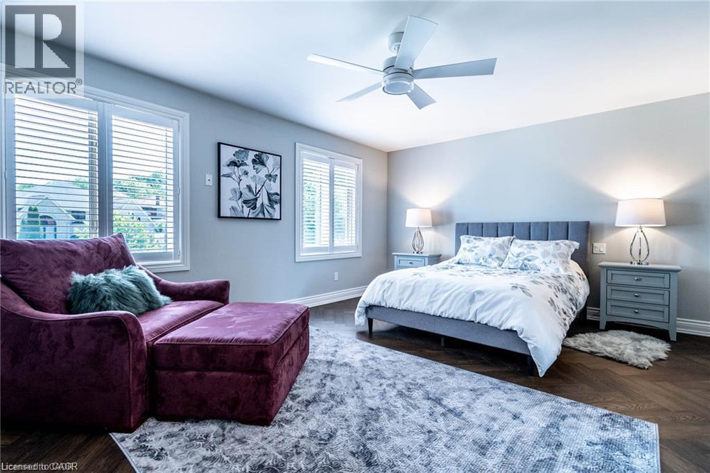 Spacious bedroom featuring wood-finish flooring, light grey walls, and two large windows with horizontal blinds - 76 Adriatic Boulevard, Hamilton, ON - Indoor Photo Showing Bedroom