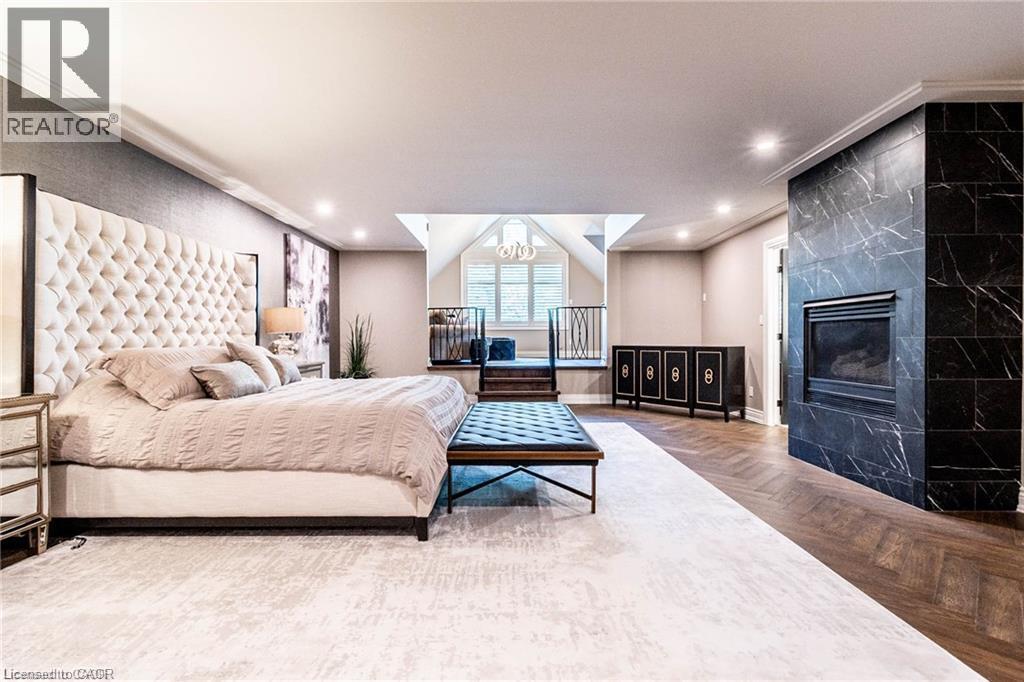 Spacious room featuring a tufted upholstered headboard, recessed lighting, and a prominent fireplace with a dark, veined tile surround - 76 Adriatic Boulevard, Hamilton, ON - Indoor Photo Showing Bedroom With Fireplace
