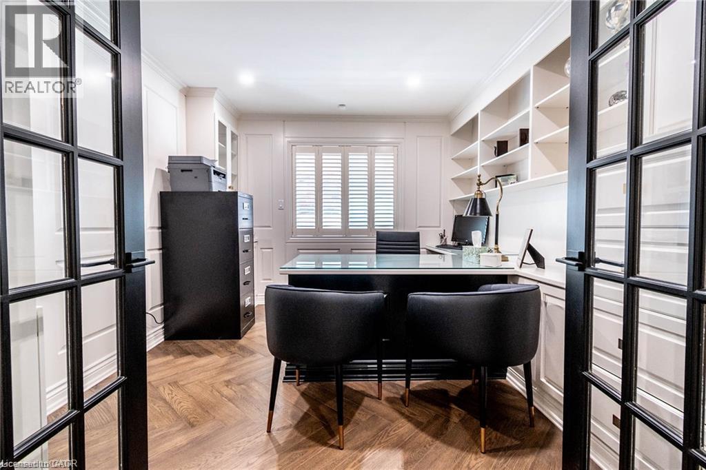 French doors with grid paneling open to a private study featuring herringbone wood-finish flooring, white built-in shelving, white wall paneling, and a window with plantation shutters - 76 Adriatic Boulevard, Hamilton, ON - Indoor