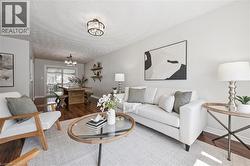Open-concept living area featuring rich wood-finish flooring, white walls, and a light-colored area rug -