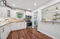 Kitchen featuring white shaker cabinetry, stainless steel appliances, wood-finish flooring, recessed lighting, and a pass-through counter -