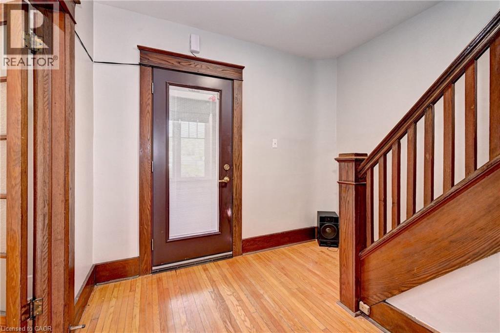 Entryway featuring wood-finish flooring, a dark wood-finish front door with an integrated window pane, rich wood-finish trim, and a wood-finish staircase with balusters - 147 Courtland Avenue E, Kitchener, ON - Indoor Photo Showing Other Room