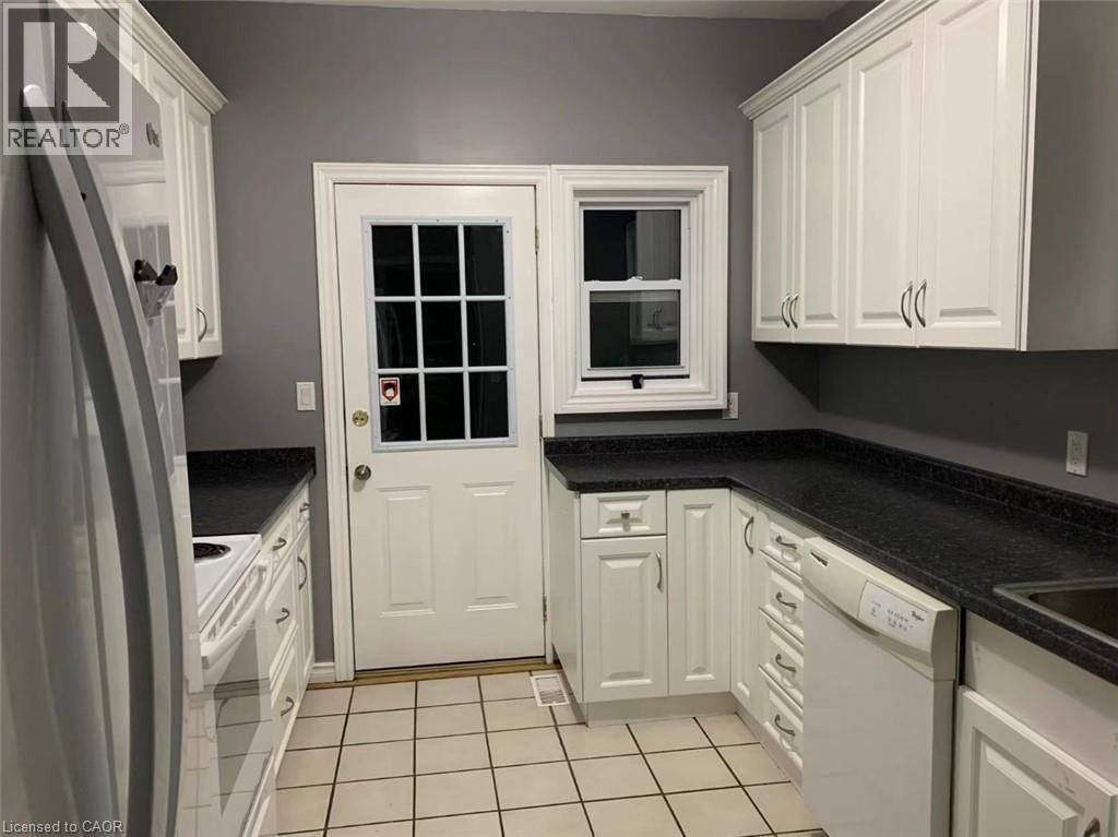 Galley kitchen featuring white cabinetry, dark countertops, white tile flooring, and a glass-paned exterior door - 1066 Richmond Street, London, ON - Indoor Photo Showing Kitchen