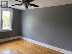 Room featuring hardwood flooring, a ceiling fan, and a window with white trim -