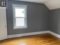 Room featuring wood-finish flooring, a double-hung window with white trim, and a high-pitched ceiling detail -