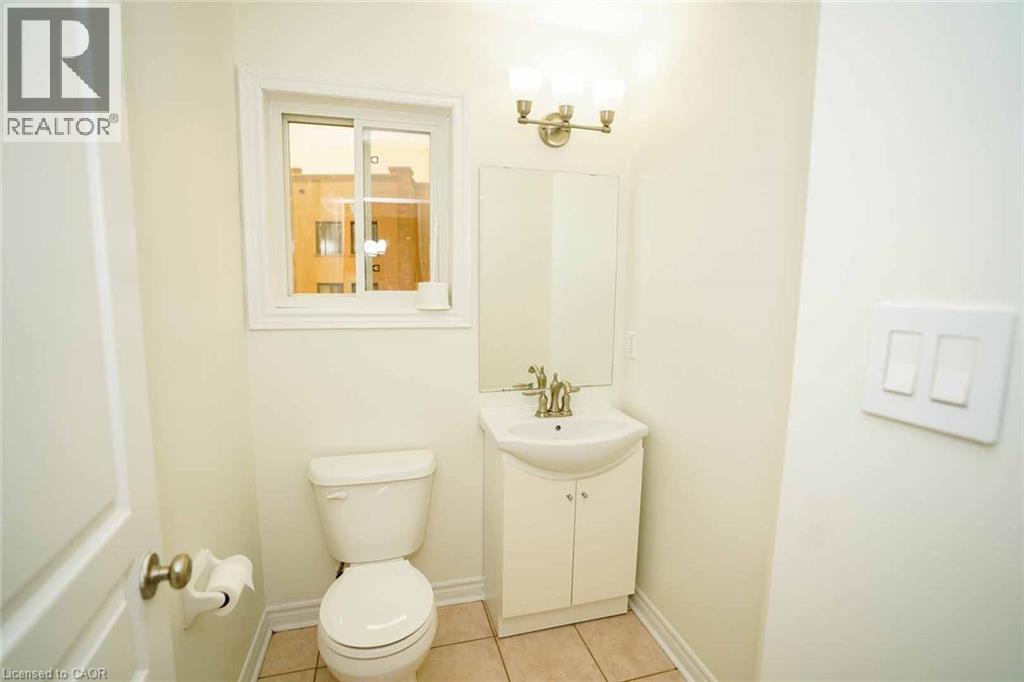 Bathroom featuring a white vanity with integrated sink, a toilet, a window with white trim, and a three-light vanity fixture - 18 Heritage Drive, Guelph, ON - Indoor Photo Showing Bathroom
