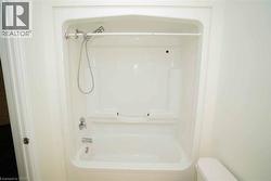 White fiberglass tub and shower combination with chrome fixtures, an integrated soap dish, and a handheld shower head -
