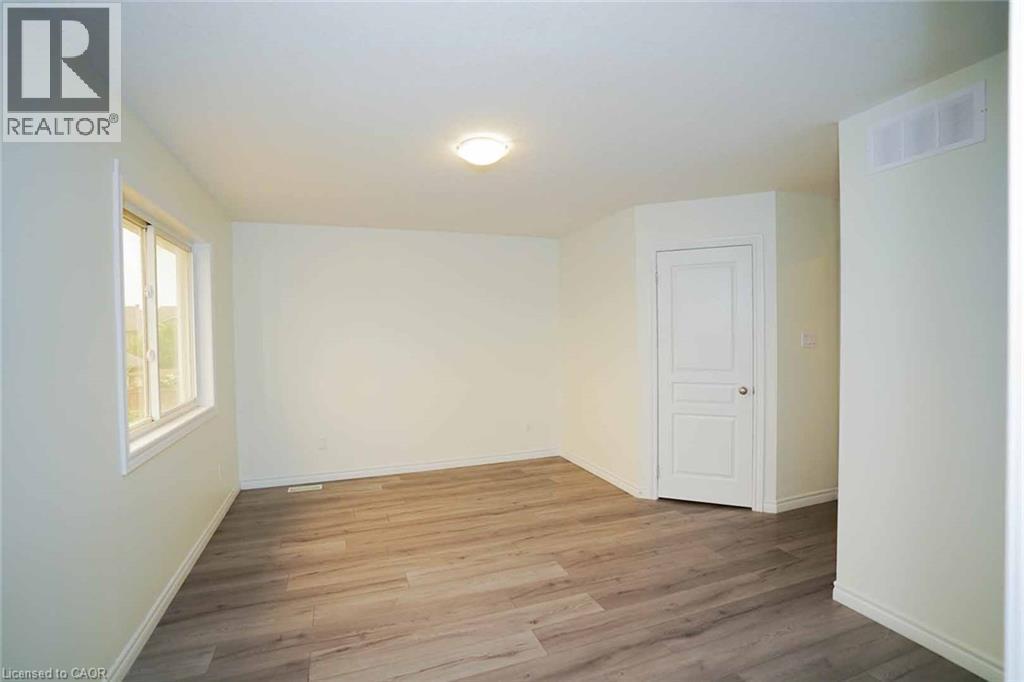 Spacious interior featuring wood-finish flooring, light-colored walls, white trim, a double-paned window, and a flush-mount ceiling light fixture - 18 Heritage Drive, Guelph, ON - Indoor Photo Showing Other Room