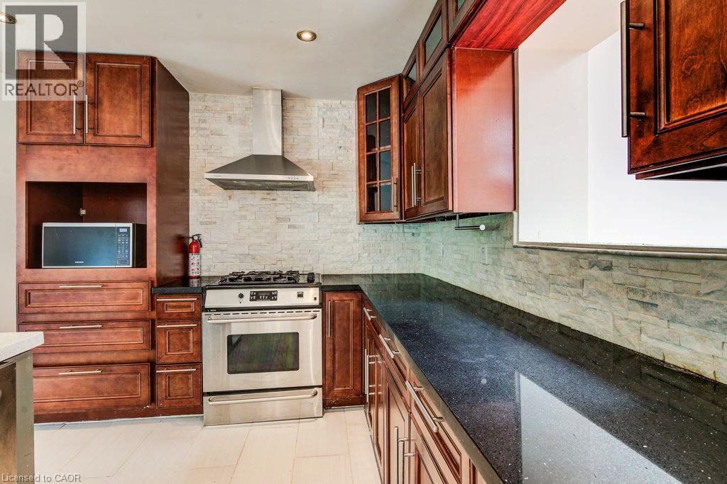 Kitchen featuring rich wood cabinetry, dark speckled countertops, stainless steel range with overhead vent, and a textured tile backsplash - 109 White Oak Place, Waterloo, ON - Indoor Photo Showing Kitchen