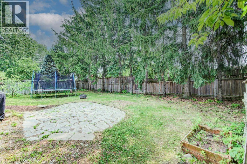 Spacious backyard featuring a stone patio, mature evergreen trees, and a raised garden bed - 109 White Oak Place, Waterloo, ON - Outdoor