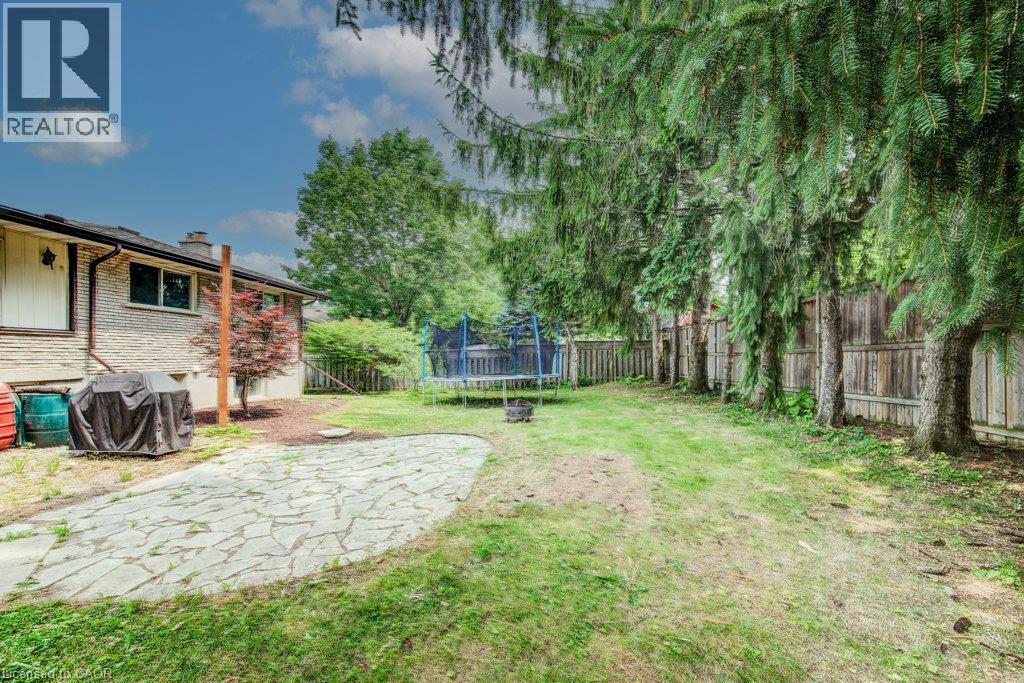 Expansive backyard featuring a natural stone patio, mature evergreen trees lining a wooden privacy fence, a manicured lawn, and a light brick exterior - 109 White Oak Place, Waterloo, ON - Outdoor