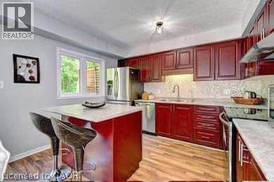 Kitchen featuring wood-finish flooring, dark wood cabinetry, white countertops, stainless steel appliances, and a window with exterior views - 175 David Bergey Drive Unit# L74, Kitchener, ON - Indoor Photo Showing Kitchen