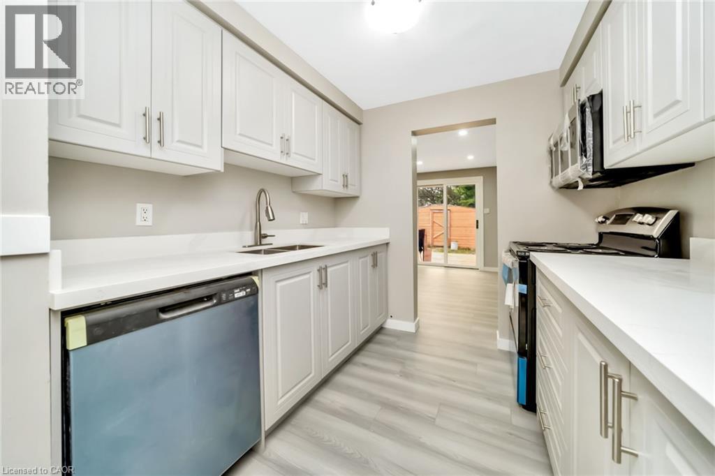 Modern kitchen featuring light gray cabinetry, white countertops, wood-finish flooring, a stainless steel sink with a gooseneck faucet, and a built-in dishwasher - 53 Burns Drive, Guelph, ON - Indoor Photo Showing Kitchen With Double Sink
