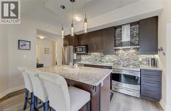 Kitchen featuring an island with granite countertop, dark wood-finish cabinetry, stainless steel appliances, and a mosaic tile backsplash -