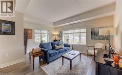 Living area featuring wood-finish flooring, two large windows with blinds, light neutral wall tones, and recessed ceiling details -