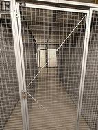 Metal mesh storage unit with a secure latch, concrete flooring, and an overhead light fixture -
