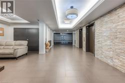Lobby area featuring light-toned large format tile flooring, stone veneer accent wall, recessed lighting, and two elevators with dark wood-finish doors -