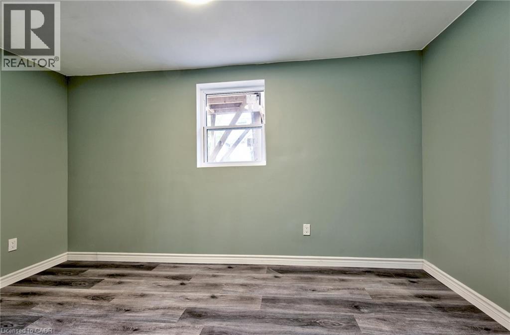 Room featuring a single-pane window, light green walls, wood-finish flooring, white baseboards, and a ceiling-mounted light fixture - 111 Gibson Avenue Unit# A, Hamilton, ON - Indoor Photo Showing Other Room