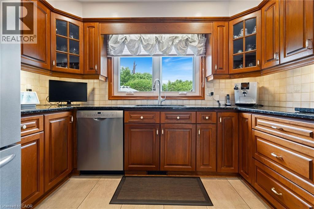U-shaped kitchen featuring wood cabinetry, dark countertops, a stainless steel dishwasher, and light tile flooring - 7 Thomson Road, Simcoe, ON - Indoor Photo Showing Kitchen