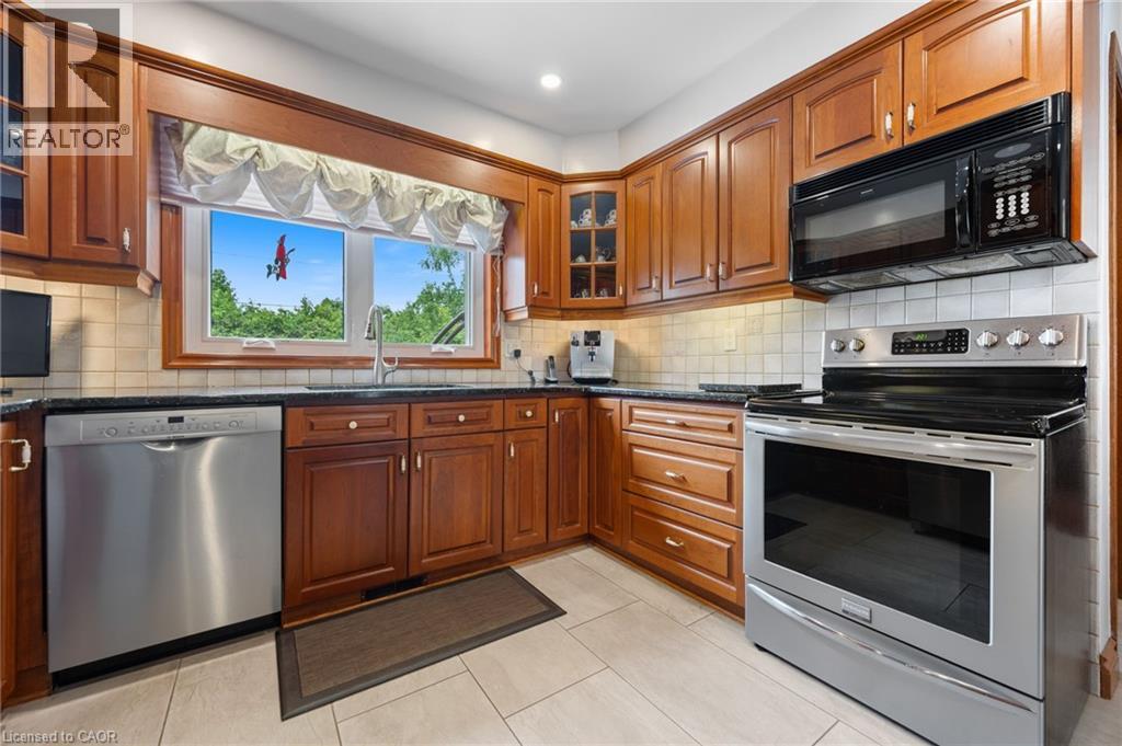 Kitchen featuring cherry wood cabinetry, stainless steel appliances, a black countertop, and a tiled backsplash - 7 Thomson Road, Simcoe, ON - Indoor Photo Showing Kitchen