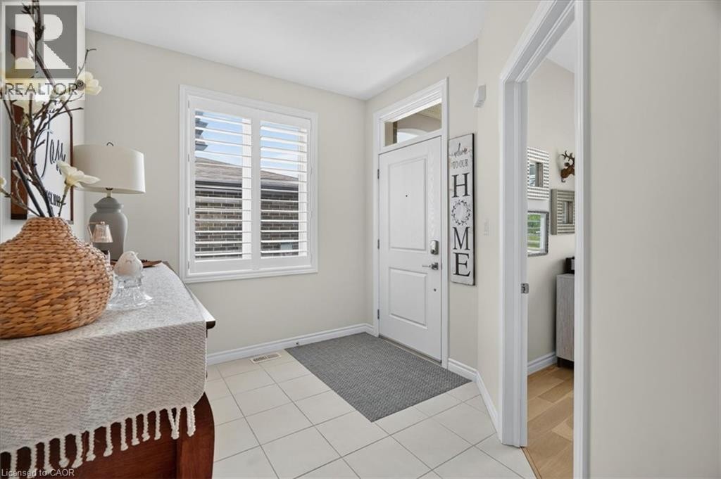Bright entryway featuring a paneled door with transom window, white plantation shutters, and light-toned square tile flooring - 87 Boyd Boulevard, Thamesford, ON - Indoor Photo Showing Other Room
