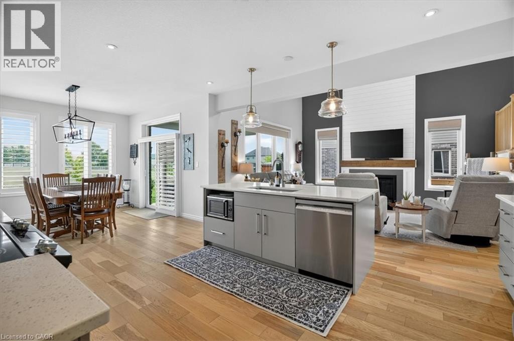 Open-concept living space featuring wood-finish flooring, a kitchen island with integrated stainless steel dishwasher, a formal dining area, and a living room with a fireplace and white shiplap accent - 87 Boyd Boulevard, Thamesford, ON - Indoor