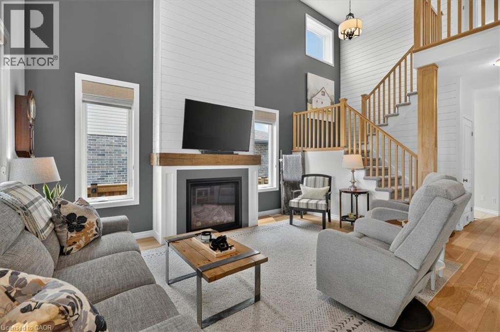 Two-story living area featuring a fireplace with a wood mantel, shiplap accent wall, hardwood flooring, and a natural wood staircase with a landing - 87 Boyd Boulevard, Thamesford, ON - Indoor Photo Showing Living Room With Fireplace