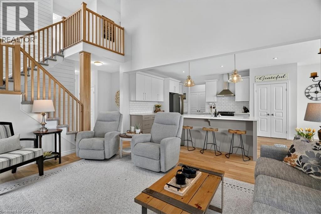 Vaulted ceiling living space featuring a stairway with wood balusters, wood-finish flooring, a kitchen island with seating, and pendant lighting - 87 Boyd Boulevard, Thamesford, ON - Indoor Photo Showing Living Room