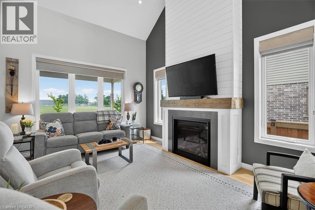 Vaulted ceiling living room featuring a floor-to-ceiling shiplap fireplace with a wood mantle, large picture windows, and light wood-finish flooring - 87 Boyd Boulevard, Thamesford, ON - Indoor Photo Showing Living Room With Fireplace