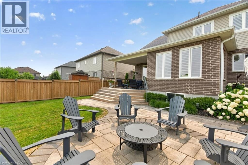Expansive paved patio with a fire pit, bordered by a manicured lawn and a wooden privacy fence - 87 Boyd Boulevard, Thamesford, ON - Outdoor With Deck Patio Veranda With Exterior