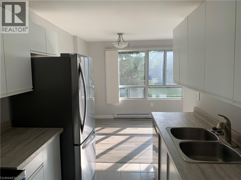Kitchen and dining area featuring wood-finish flooring, white cabinetry, and a double basin sink - 65 Highland Crescent Unit# 201, Kitchener, ON - Indoor Photo Showing Kitchen With Double Sink