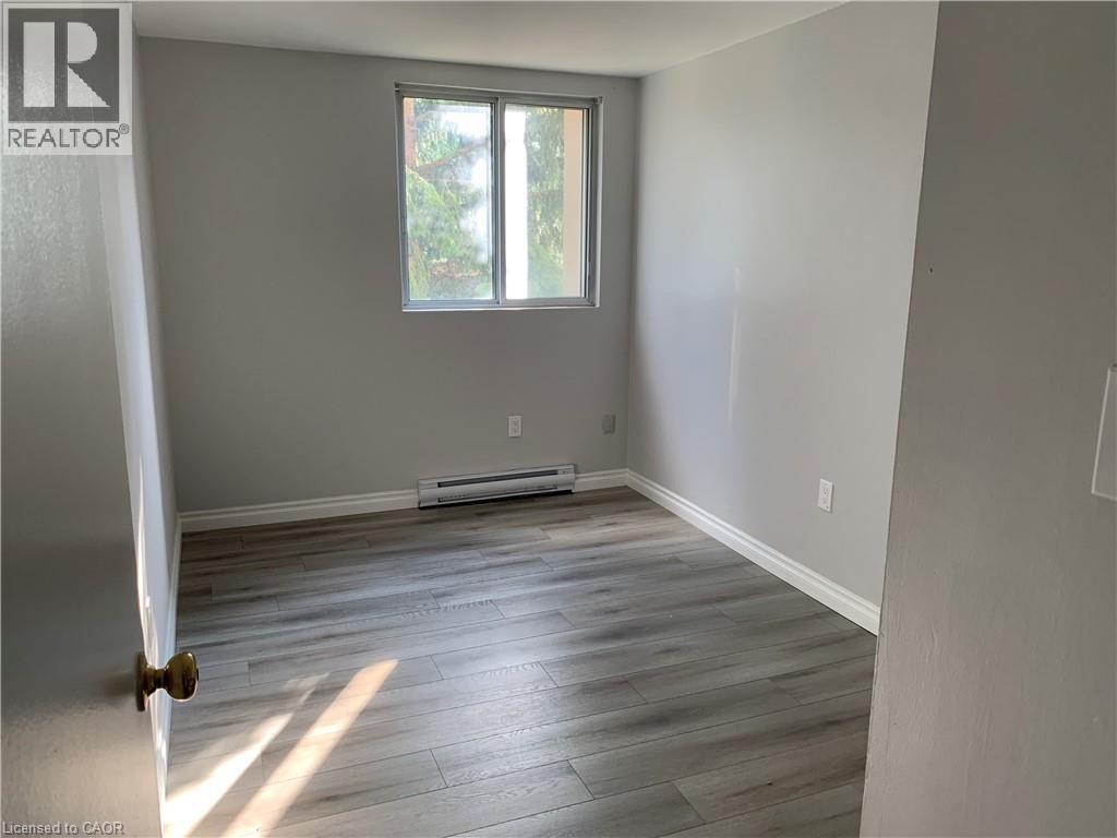 Room featuring light gray walls, wood-finish flooring, white baseboards, and a window providing natural illumination - 65 Highland Crescent Unit# 201, Kitchener, ON - Indoor Photo Showing Other Room