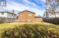Expansive grassy backyard featuring a brick exterior, multiple windows, a wooden deck, and a wood privacy fence -