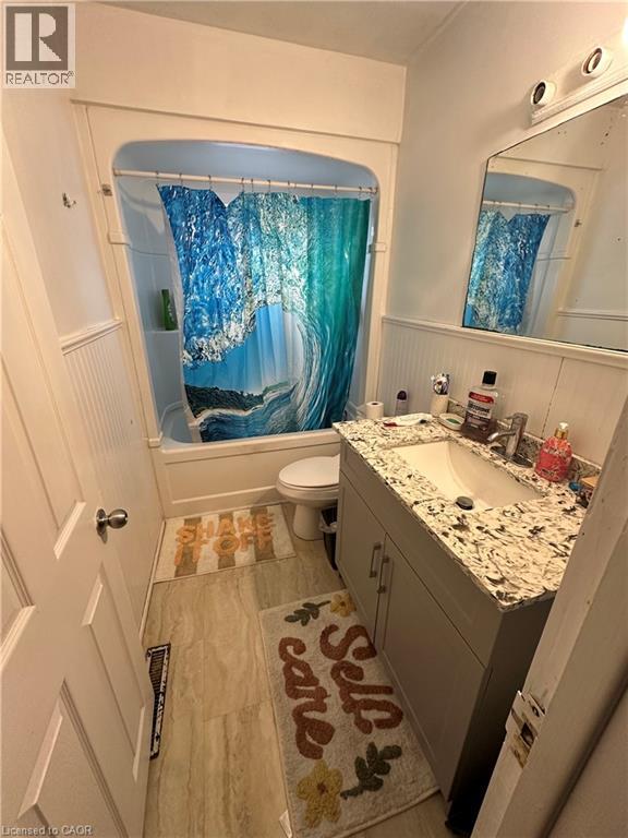 Bathroom featuring a built-in tub with a shower, a vanity with a light-toned countertop and an integrated sink, and wood-finish flooring - 240 West 2Nd Street, Hamilton, ON - Indoor Photo Showing Bathroom