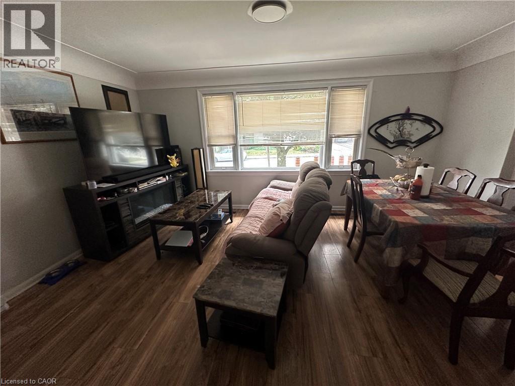 Open-concept living and dining area featuring wood-finish flooring, a broad window with blinds, and a ceiling-mounted light fixture - 240 West 2Nd Street, Hamilton, ON - Indoor Photo Showing Other Room