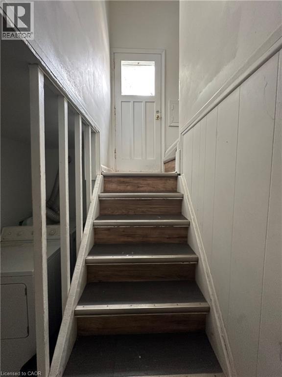 Staircase with wood-finish treads, black step inserts, and metal trim leading to a white door with a window pane - 240 West 2Nd Street, Hamilton, ON - Indoor Photo Showing Other Room