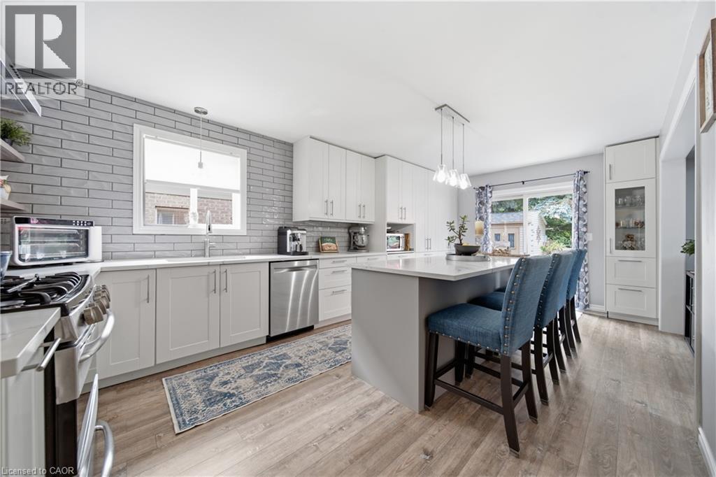 Modern kitchen featuring a central island with seating, extensive white cabinetry, stainless steel appliances, light wood-finish flooring, and a gray subway tile backsplash - 79 Beaverbrook Crescent, Cambridge, ON - Indoor