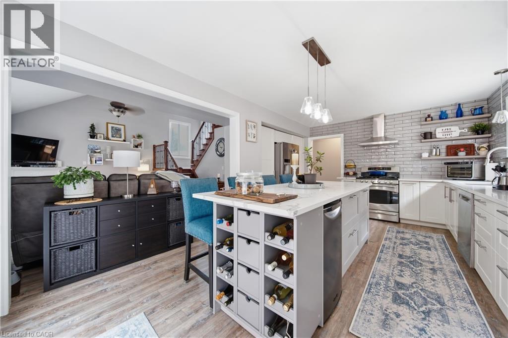 Kitchen featuring a large central island with integrated wine storage, white cabinetry, stainless steel appliances, a gray brick-patterned backsplash, and wood-finish flooring - 79 Beaverbrook Crescent, Cambridge, ON - Indoor Photo Showing Kitchen With Upgraded Kitchen