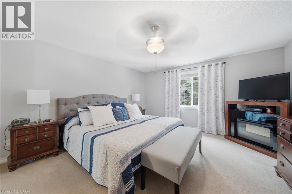 Carpeted bedroom featuring light gray walls, a ceiling fan with integrated lighting, a window with curtains, and a built-in media console with an electric fireplace - 79 Beaverbrook Crescent, Cambridge, ON - Indoor Photo Showing Bedroom