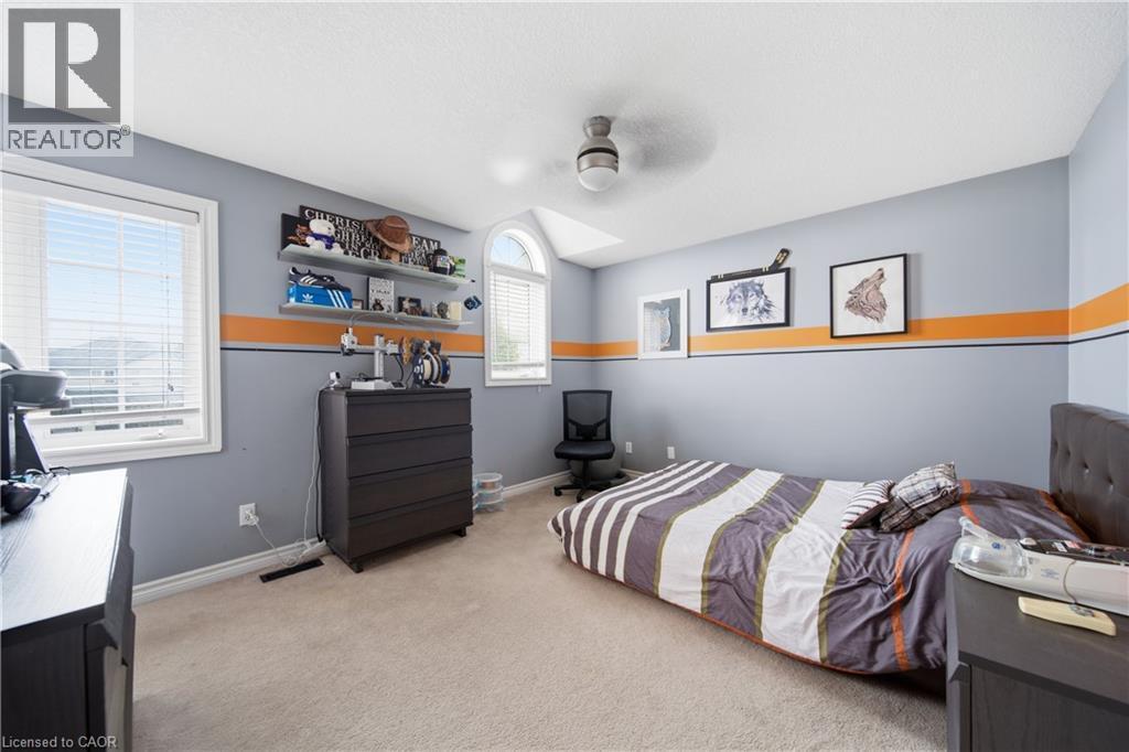 Carpeted room featuring dual windows, including an arched transom window, a ceiling fan with integrated lighting, and multiple wall-mounted shelves for display - 79 Beaverbrook Crescent, Cambridge, ON - Indoor Photo Showing Bedroom