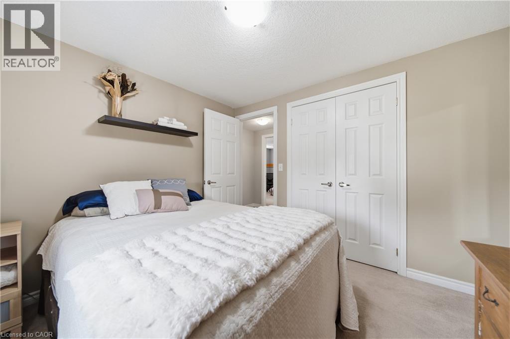 Neutral-toned room featuring a single panel ceiling light, textured ceiling, a floating wall shelf, two paneled closet doors, and a paneled interior door - 79 Beaverbrook Crescent, Cambridge, ON - Indoor Photo Showing Bedroom