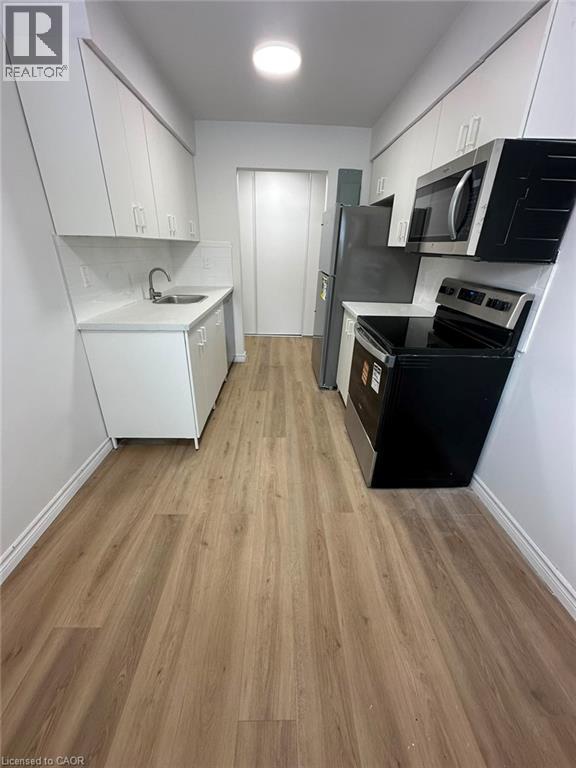Galley kitchen featuring wood-finish flooring, white cabinetry, integrated stainless-steel appliances, white countertops, and a subway tile backsplash - 145 Macgregor Crescent Unit# 8 (R1), Waterloo, ON - Indoor Photo Showing Kitchen