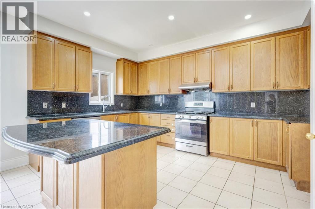 Kitchen featuring a central island with a dark stone countertop, extensive light wood cabinetry, a stainless steel range with overhead ventilation, and tiled flooring - 5 Freshspring Drive, Brampton, ON - Indoor Photo Showing Kitchen