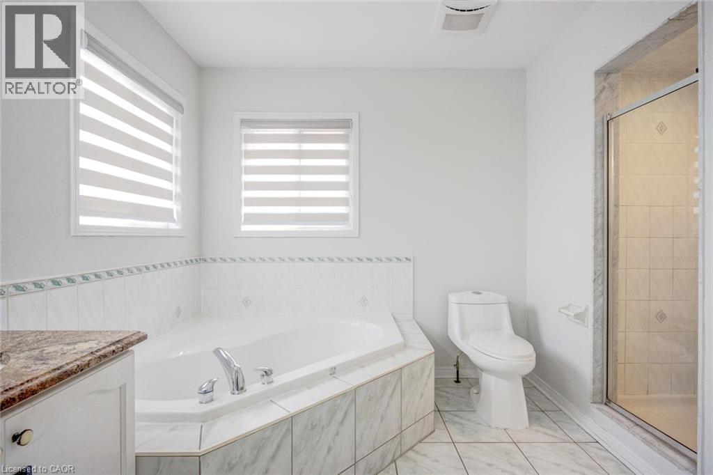 Corner soaking tub with tiled surround, dual windows with blinds, walk-in shower with glass enclosure, toilet, and a vanity with a granite-finish countertop - 5 Freshspring Drive, Brampton, ON - Indoor Photo Showing Bathroom
