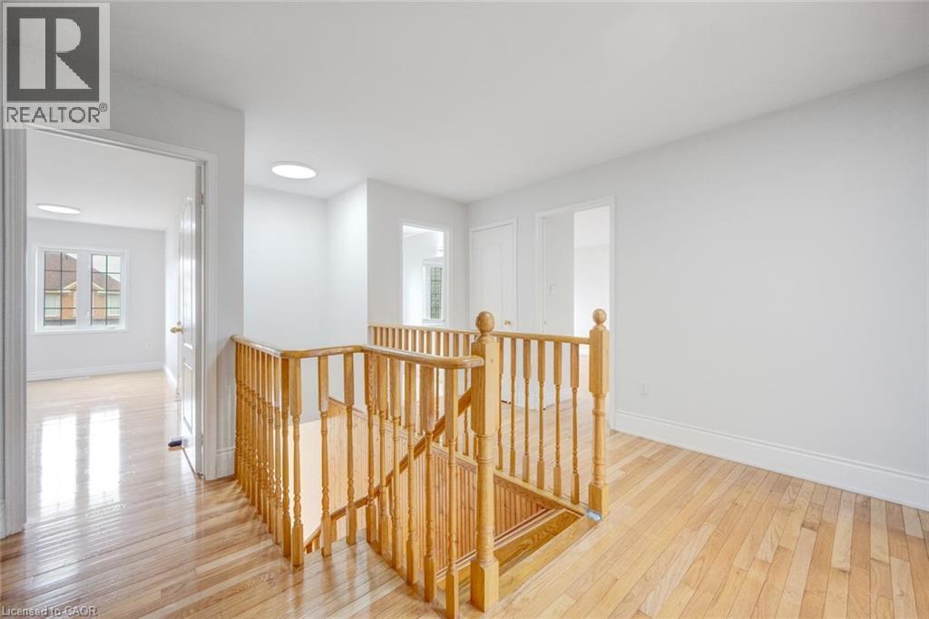 Hardwood flooring throughout a bright upper-level hallway featuring a wooden staircase and balusters, multiple doorways, and recessed lighting - 5 Freshspring Drive, Brampton, ON - Indoor Photo Showing Other Room